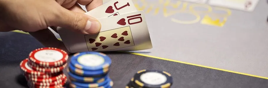 En hand som håller upp två kort under ett poker-spel med pokermarker på sidan om